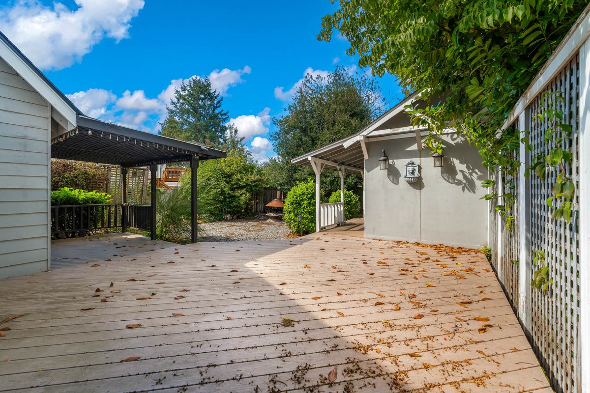 Backyard wood deck with a covered pergola, lattice screening, and garden beyond